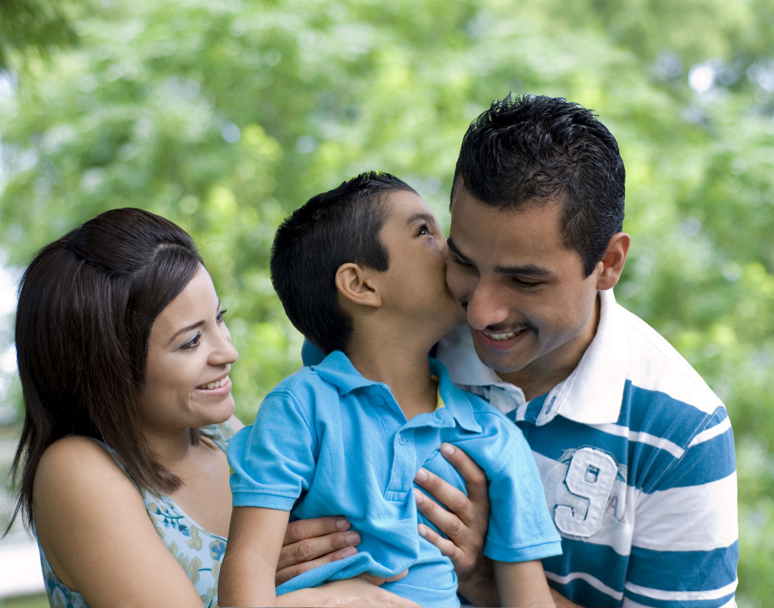 A young boy kisses his father on the cheek while his mother smiles warmly beside them. This joyful family moment captures the love, unity, and support that Casa Esperanza aims to cultivate within the Latine community.