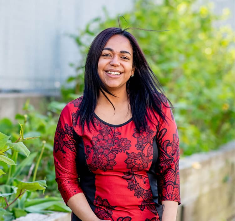 A smiling woman standing outside in a garden, representing the positive and supportive community at CasaCare, where personalized wellness plans are provided.