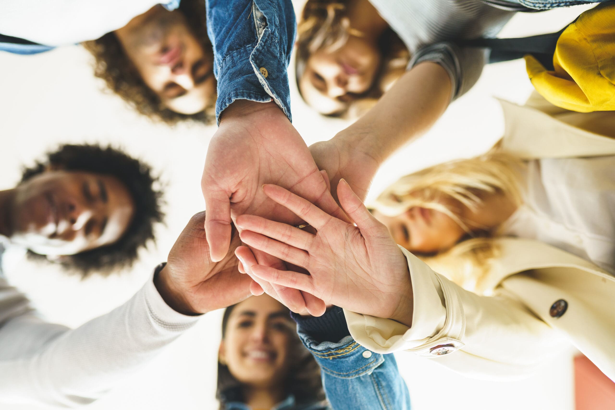 Hands of a multi-ethnic group of friends joined together as a sign of support and teamwork. Young people having fun together.