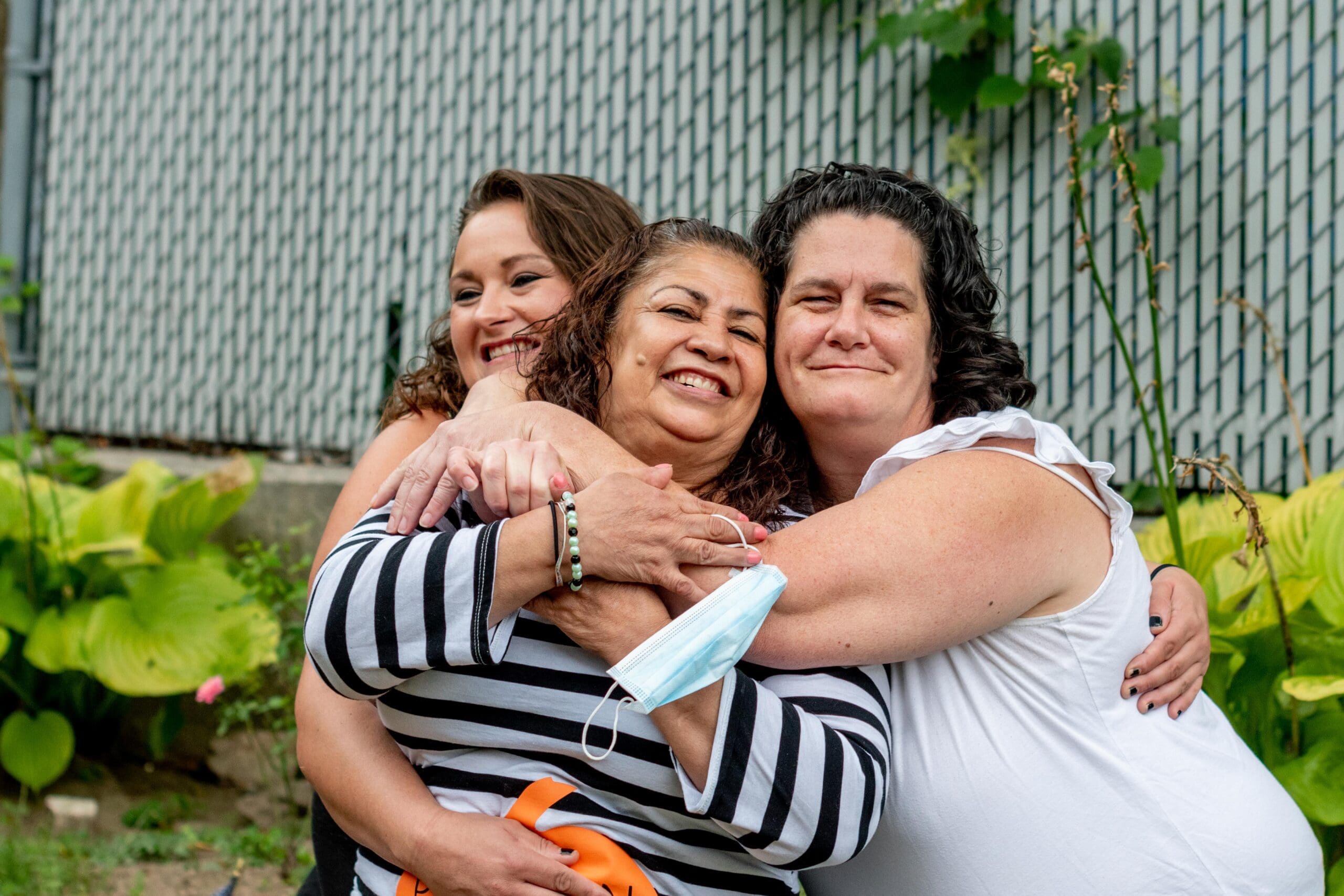 Three women embrace tightly, smiling and radiating joy, symbolizing care and resilience in the face of challenges.